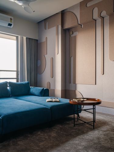 Teal sectional sofa before a sculptural beige relief wall with a round wood tray table
