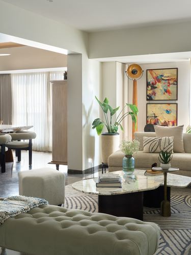 Living room with beige sofa, marble coffee table, arc lamp and abstract paintings on cream walls