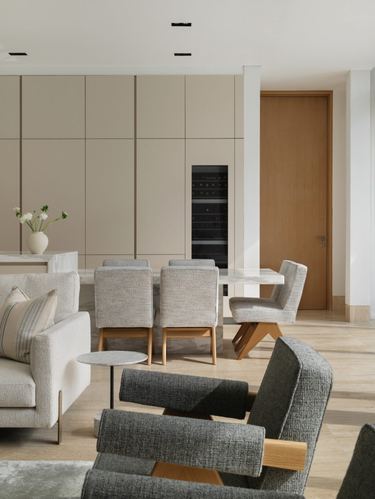 Open living-dining space with stone table, grey boucle armchairs and panelled cabinetry wall