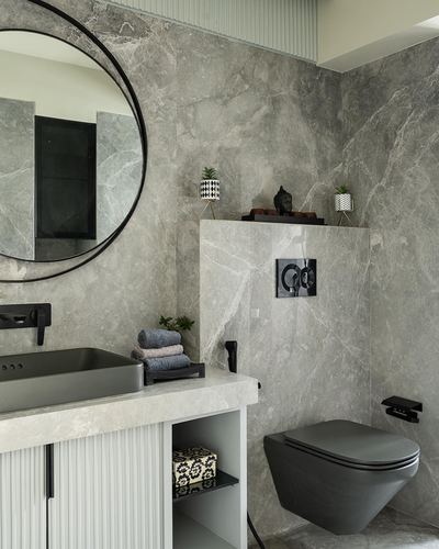 Grey stone bathroom with round mirror, vessel sink, and matte black wall-hung toilet
