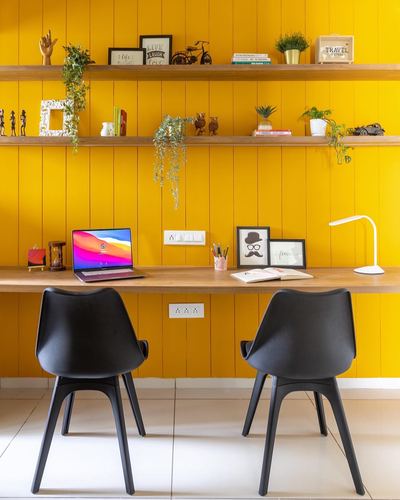 Study nook with mustard wood-paneled wall, floating shelves, wooden desk and two black chairs