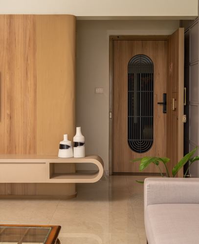 Foyer view of a fluted wood panel wall, floating console with vases, and an arched-grille wooden main door