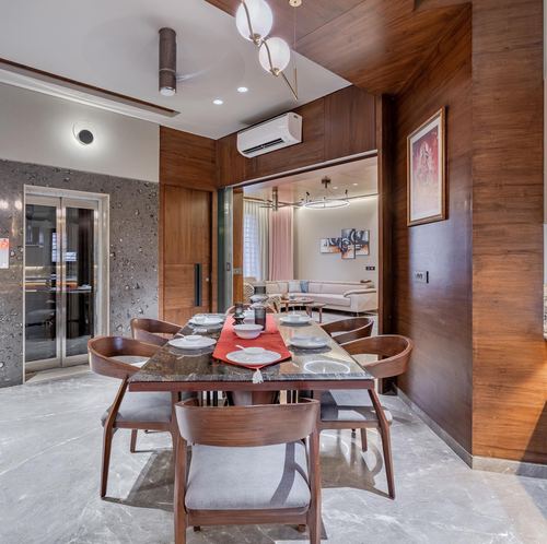 Wood-panelled dining room with marble table set for a meal, opening into a living room beyond