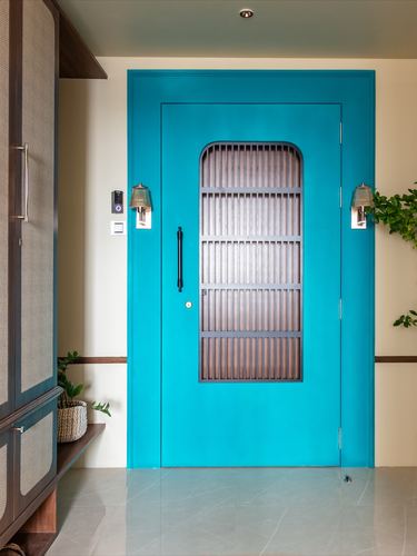 Teal entry door with wooden slatted grille panel flanked by wall sconces in a marble-floored foyer