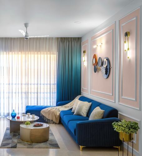 Blue velvet sectional sofa against blush pink paneled wall with brass sconces and decorative plates