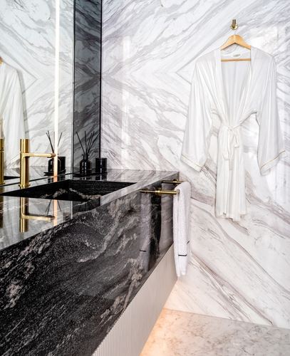 White marble bathroom with black veined stone counter, brass fittings, and white robe hanging on hook