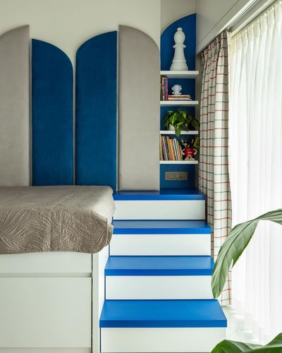 Kids bedroom corner with arched blue and grey velvet panels and blue-white built-in storage steps by a window