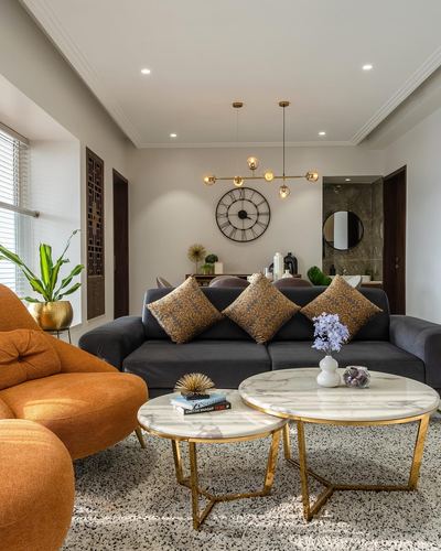Living room with orange sofa, charcoal sectional, gold nesting marble tables and a large wall clock