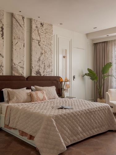 Beige bedroom with dark upholstered bed, marble wall panels, and herringbone wood floor