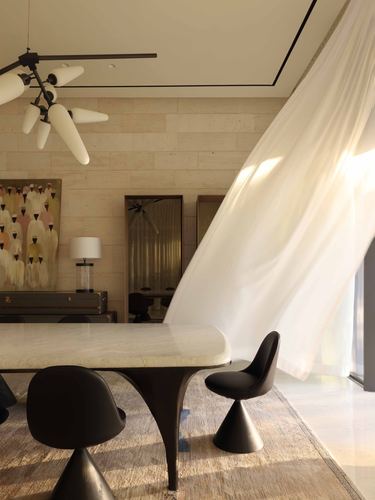 Dining area with stone wall, marble table, dark cone chairs, and a curtain caught mid-billow in sunlight