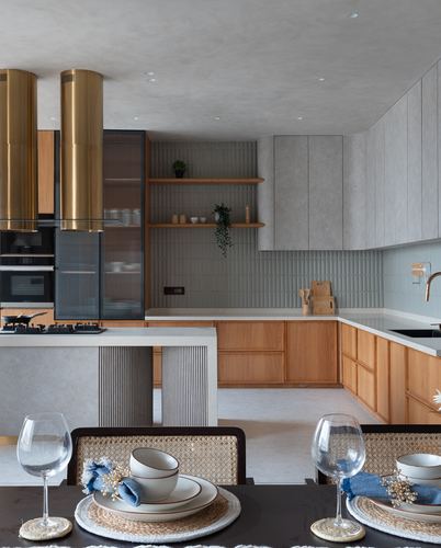 Contemporary kitchen with brass cylindrical hoods, wood cabinetry, and a set dining table in foreground