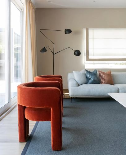 Two curved orange velvet chairs in front of a light sofa with a sculptural black floor lamp