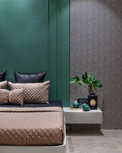 Bed with taupe quilted bedding against green wall, floating nightstand with plant and vase beside fluted panel