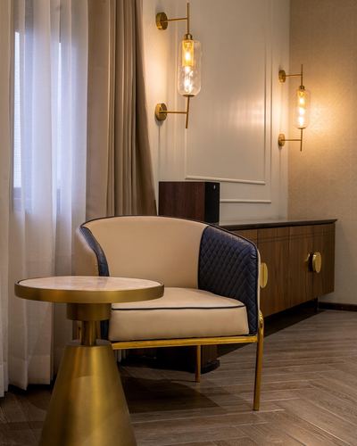 Cream and navy quilted armchair beside a brass marble-top table under glowing brass wall sconces