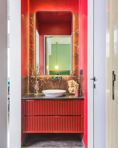 Red powder room with backlit marble mirror niche and ribbed red fluted vanity with oval sink