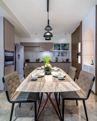 Marble dining table set for four beneath layered pendant lights, open kitchen behind