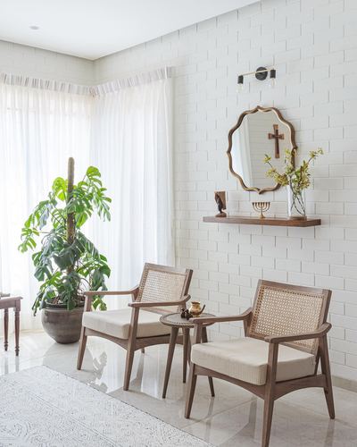 Two cane-backed wooden armchairs face a white brick wall with a scalloped mirror and floating shelf