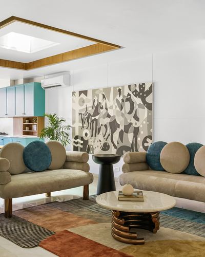Living room with two beige velvet sofas, teal bolsters, patterned wall art, and marble coffee table