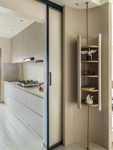 Beige kitchen with fluted sliding door beside a curved wall with circular brass display shelves