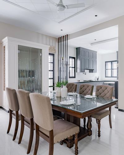 Formal dining room with glass-top wood table, tufted chairs, and view into grey kitchen beyond