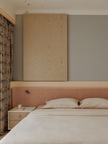 Bedroom with wood panel above pink upholstered headboard and floral curtain