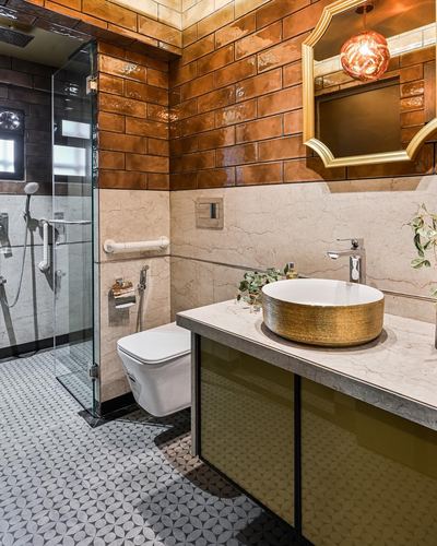 Bathroom with glossy terracotta tile walls, marble counter, gold vessel sink, arched mirror