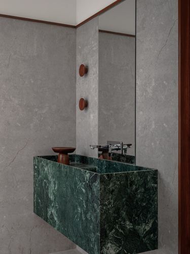 Green stone floating vanity beneath mirror in grey stone bathroom with wooden accents