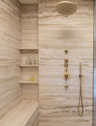 Travertine-clad shower corner with brass rain shower head, valve, and built-in stone shelves