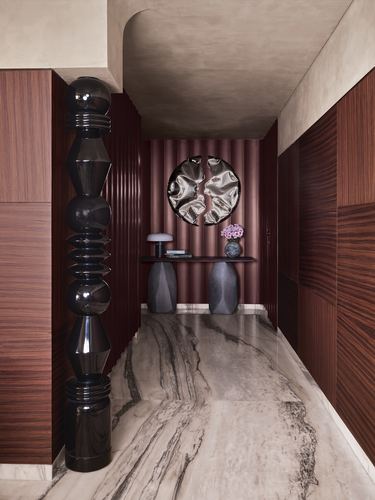 Marble-floored corridor with dark wood veneer walls, fluted maroon paneling, and a sculptural black totem column