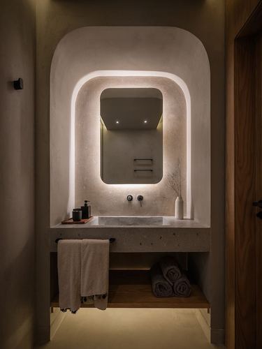 Arched plaster niche bathroom with backlit mirror over a stone vanity, warm ambient light