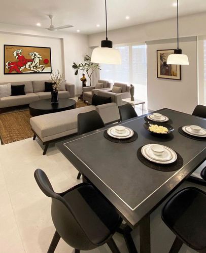 Open living-dining space with black dining table under pendant lights and grey sofas beyond