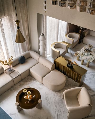 Elevated view of a beige living room with curved sofas, brass console, and marble floor beneath a mezzanine screen
