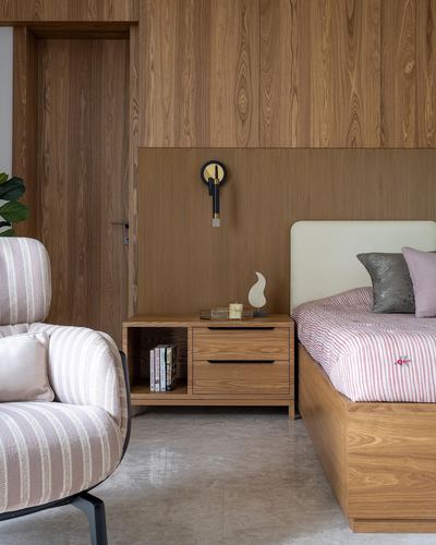 Wood-paneled bedroom corner with nightstand, brass sconce, and upholstered bed with pink linens