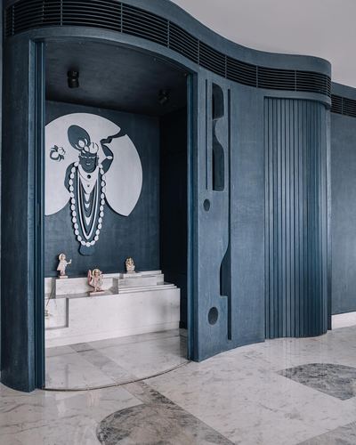 Curved blue fluted wall opens to a pooja room with a painted deity mural and marble platform