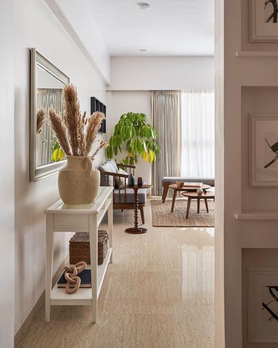 Foyer with console table and vase leading to sunlit living room down a marble hallway