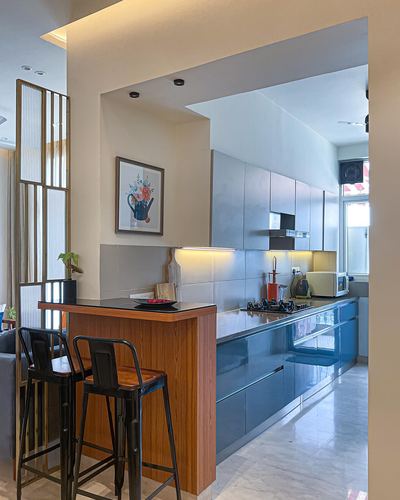 Blue glossy kitchen with wooden breakfast counter and two black stools, marble flooring
