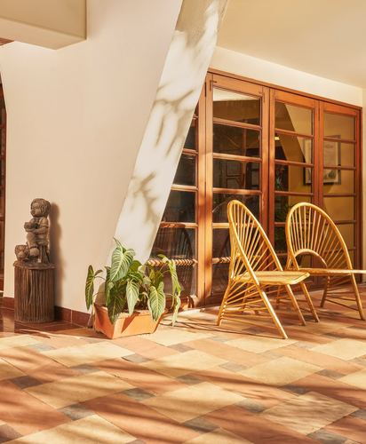 Sunlit balcony with rattan chairs, wooden statue, and patterned terracotta tile floor