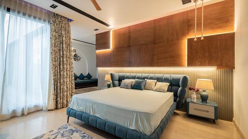 Bedroom with teal tufted bed against backlit wood panelled wall and sheer curtained window
