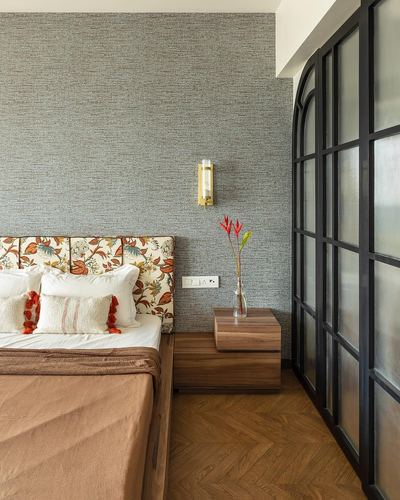 Bedroom with floral headboard, walnut nightstand, brass sconce and arched glass partition wall
