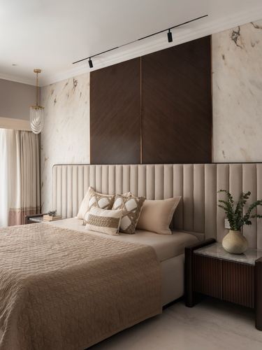 Beige upholstered ribbed headboard bed beneath dark wood panel on marble wall, bedside table with vase