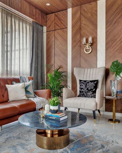 Living room corner with chevron wood paneling, leather sofa, tufted armchair, and round marble-top coffee table