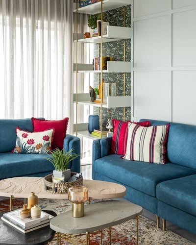Blue velvet sofas with red and white striped pillows around layered stone-top coffee tables in a colorful living room