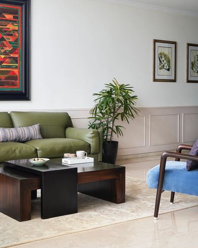 Living room with olive green sofa, dark wood nesting tables, and framed art above paneled walls