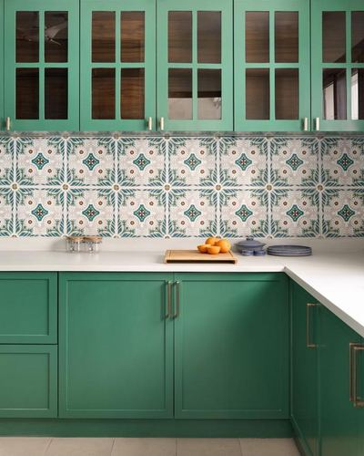 Green kitchen with patterned tile backsplash, white countertop, oranges on cutting board, brass handles