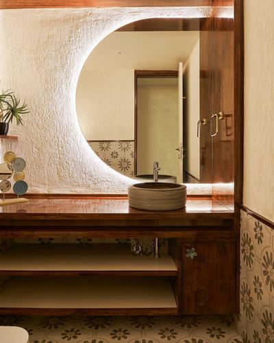 Bathroom vanity with round vessel sink under a circular backlit mirror on textured plaster wall