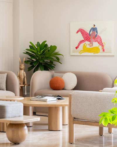 Beige living room with sofas, round wood coffee table, plant, and colorful equestrian painting