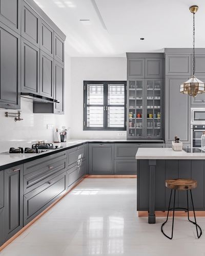 Grey shaker-style kitchen with white countertops, glass cabinets, copper trim, and central island with wooden stool