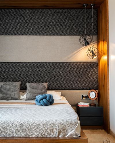Bedroom corner with striped fabric headboard, wire pendant lights, and blue knot cushion on bed.