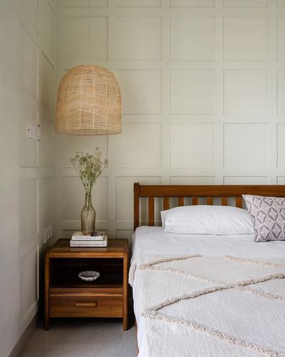 Bedroom corner with woven pendant lamp, wooden nightstand, and panelled sage wall beside a wooden bed
