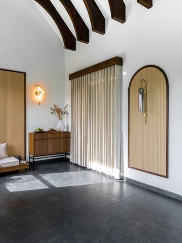 Foyer with sloped beamed ceiling, arched fluted niche, wooden console and dark stone floor